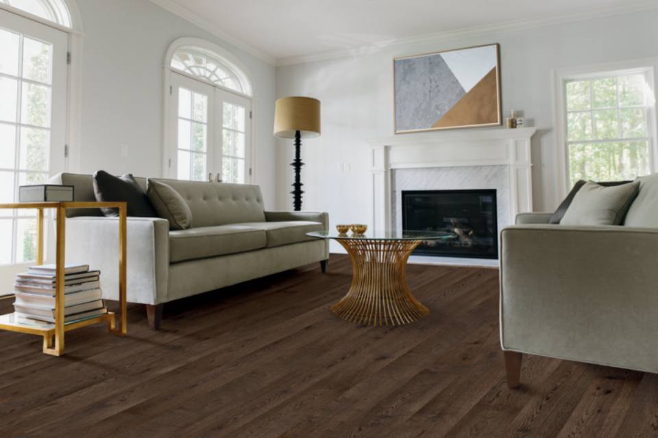 Dark hardwood flooring in living room with grey couches and gold accent furniture.